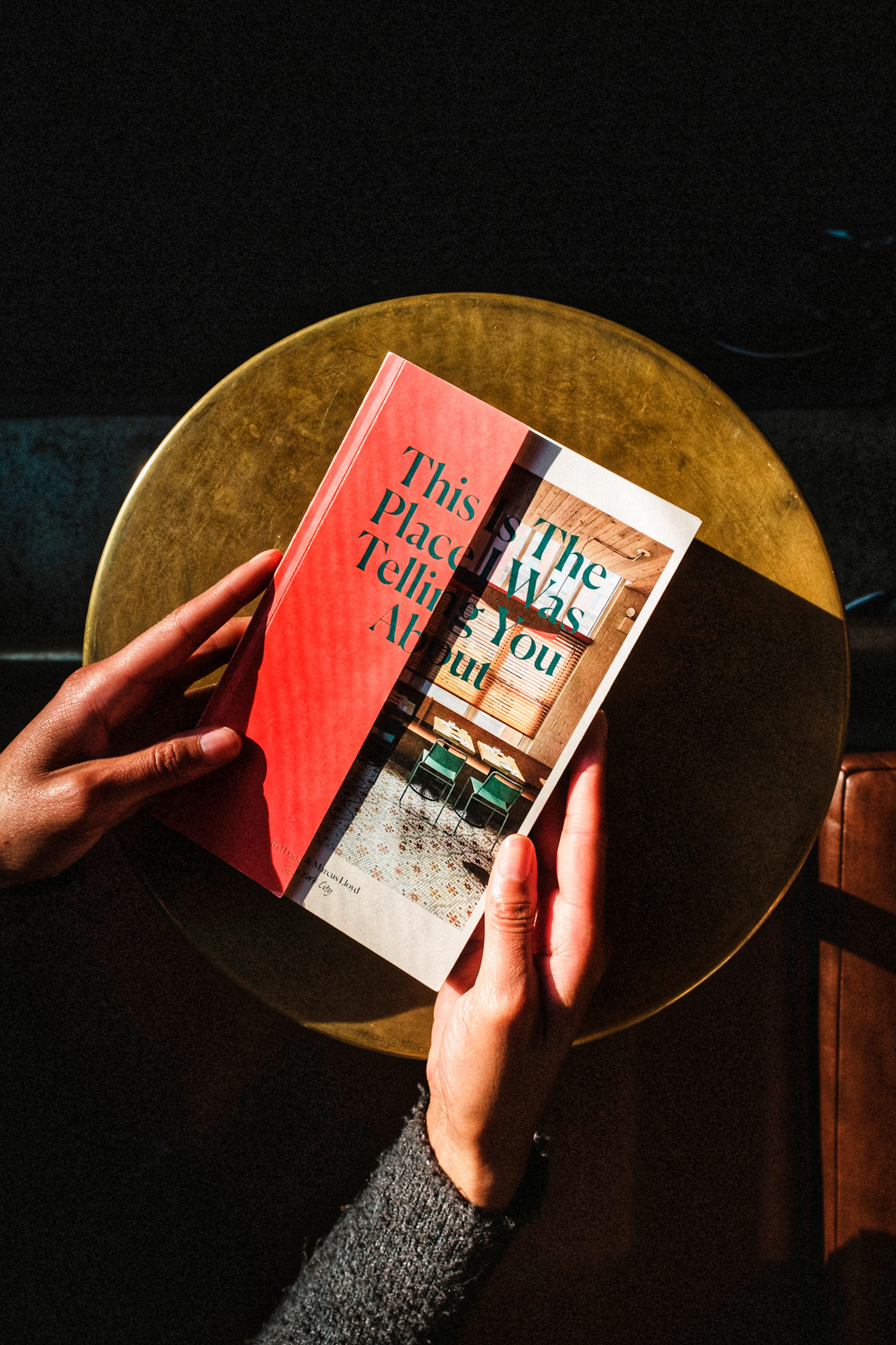 Hands holding the book showing the red book cover with the title This is The Place I Was Telling You About written across it.
