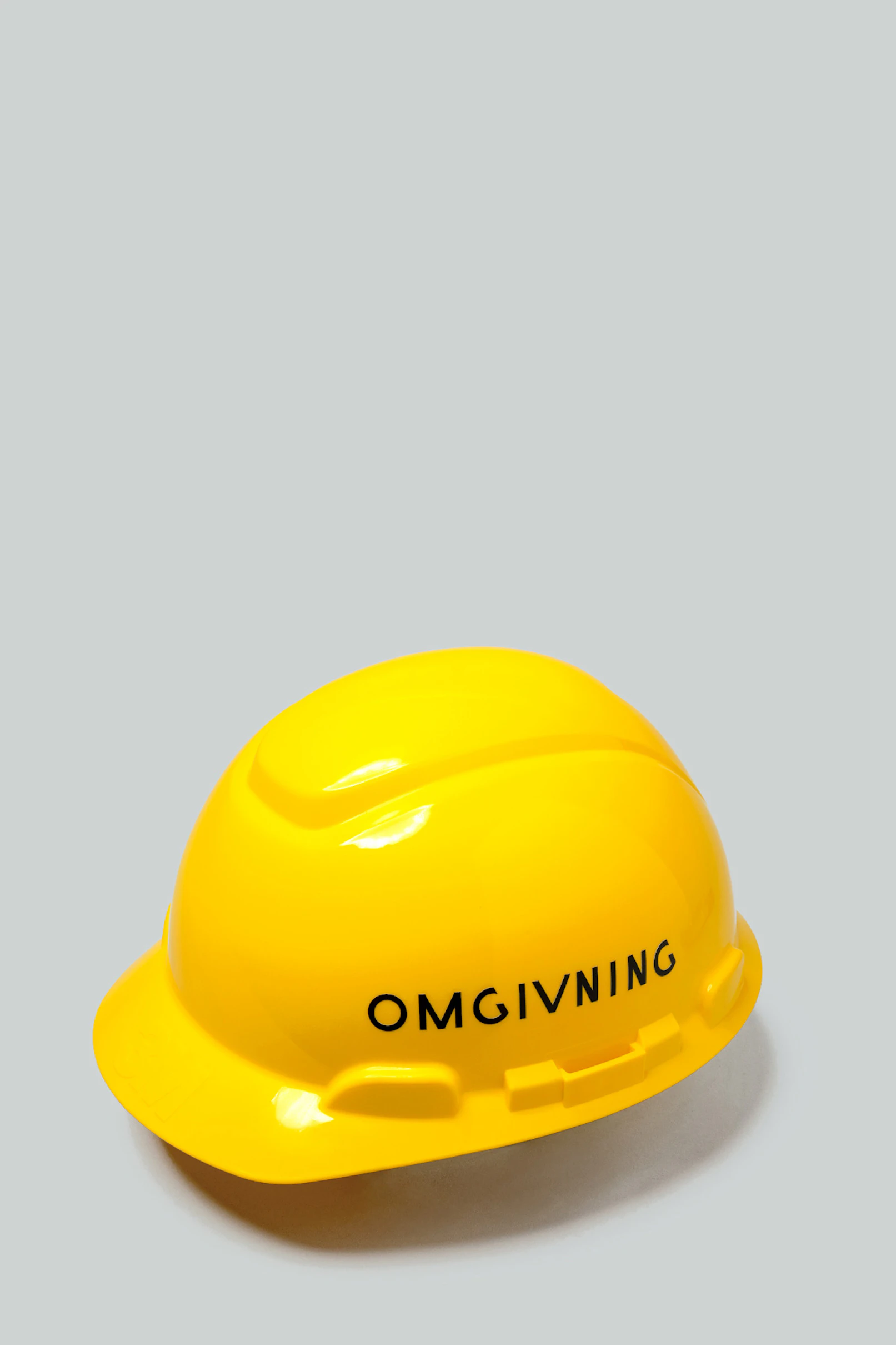 Bright yellow hardhat with Omgivning written in black on the side.