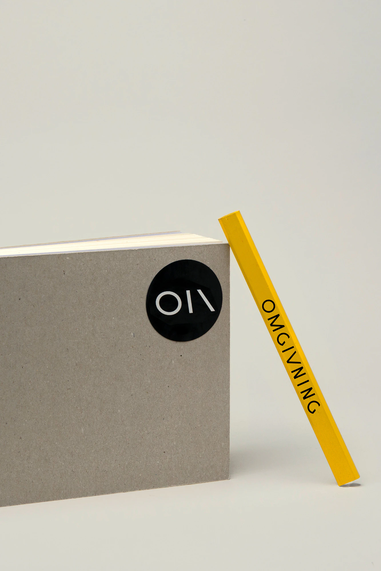 Photo showing a notebook and a yellow pencil, both with the brand logo in black.