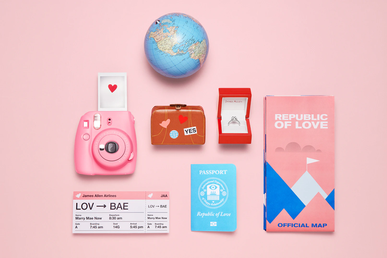 Image showing branded traveling items - a plane ticket, a map, a mini suitcase, a passport, a globe, and a polaroid camera, and an open ring box with an engagement ring inside. All with references to getting married and all against a soft pink seamless.