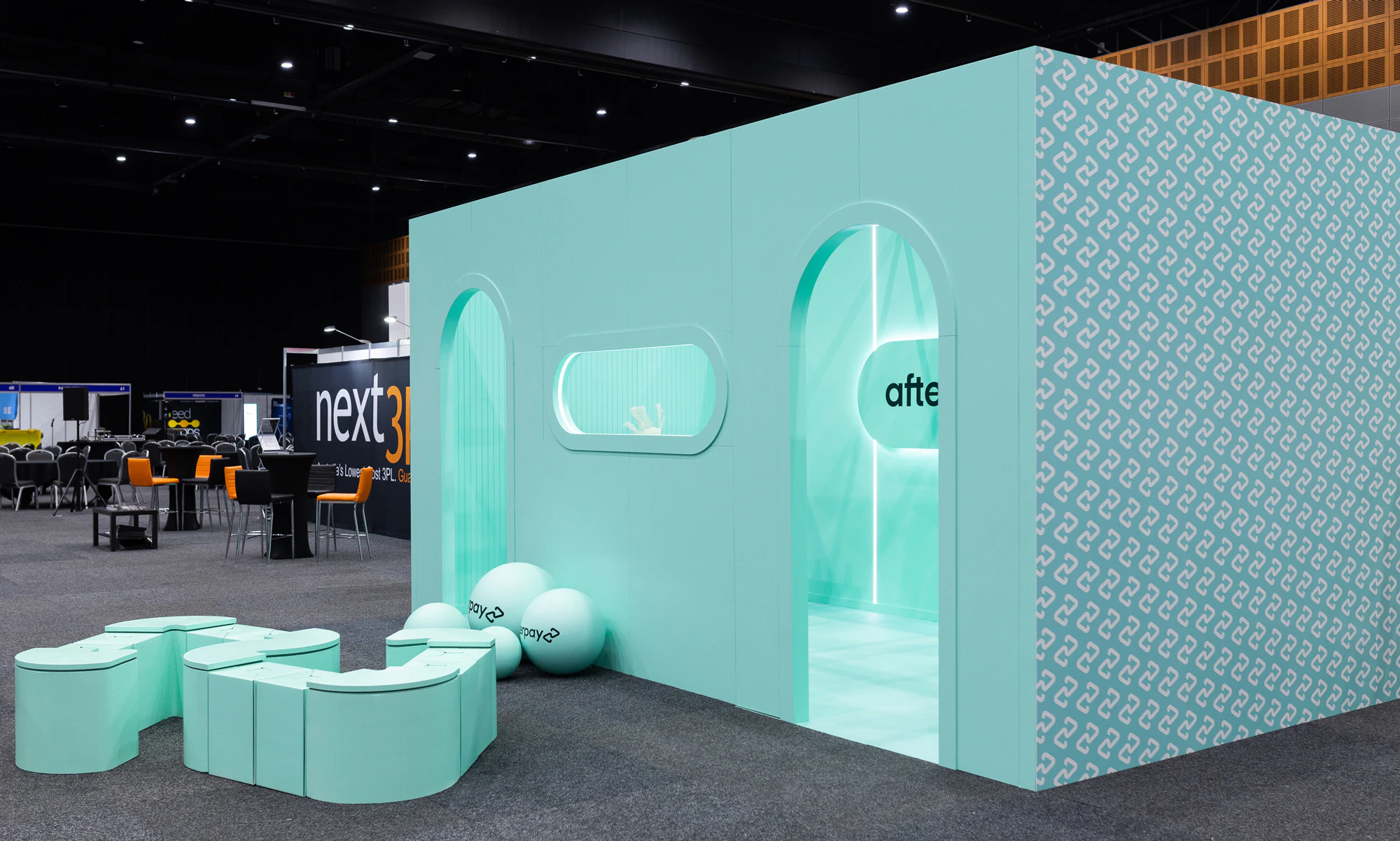 Image showing the Afterpay Bondi Mint expo stand from the outside. The main stand is a mint box with two arched entryways and the sides have the logo printed in white as an all over pattern. In between the two entryways there are large mint spheres with the Afterpay logo in black printed on them and there is an oversized mint logo where people can sit. The rest of the expo is black and gray making the mint booth really stand out.