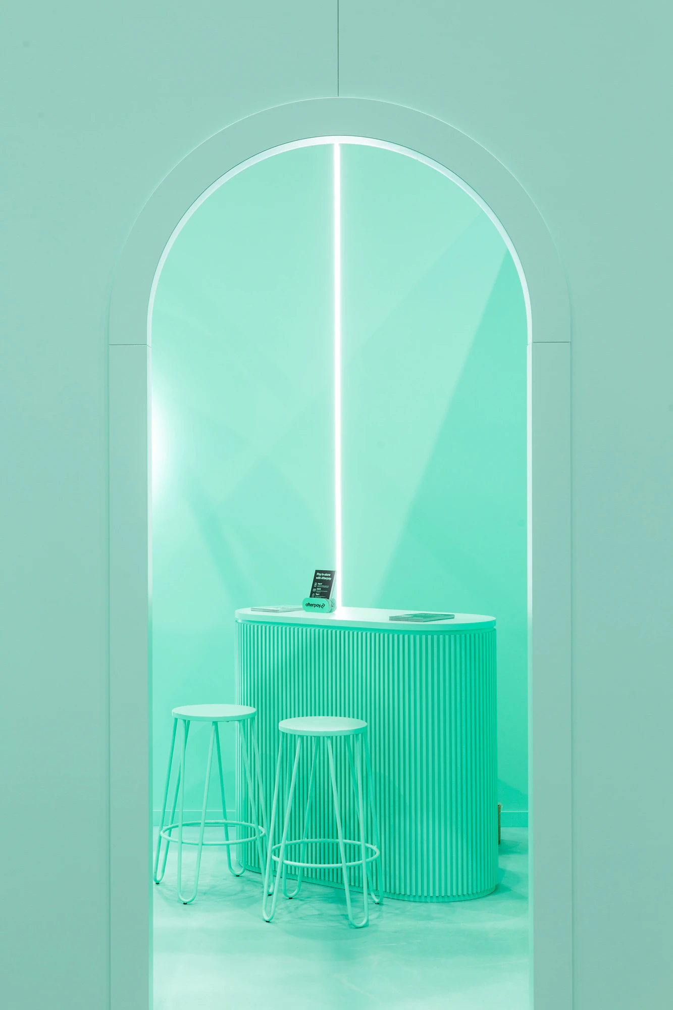 Image showing one of the two arched entrances to the Afterpay Bondi Mint expo booth. Looking through the entrance we can see a tall mint desk with two mint stools in front of it. On top of the desk are black pamphlets explaining Afterpay.