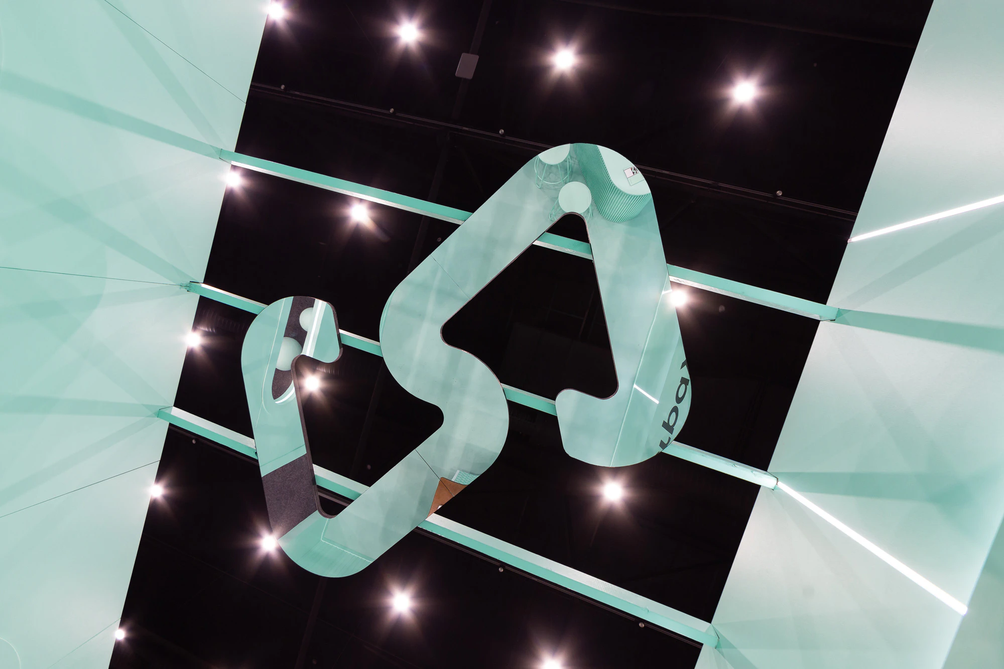 Image showing the ceiling of the Afterpay Bondi Mint expo booth. There is an oversized mirror version of the logo reflecting the mint booth and behind the mirror logo there is the black ceiling of the expo hall with spot lights looking like stars.