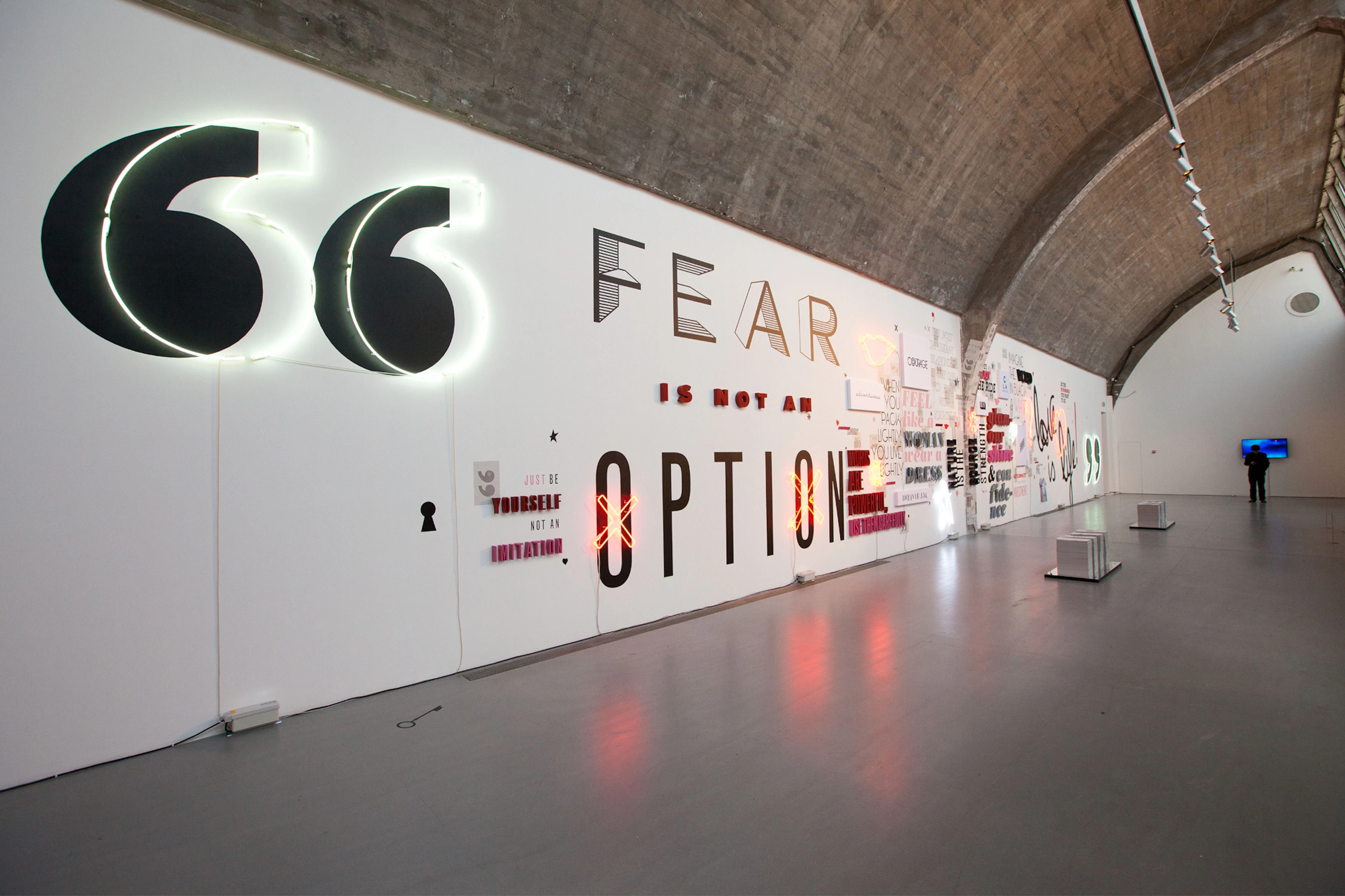 Image showing a very long wall inside the Pace Gallery. The wall is white and on top of it is the beginning of the DVF quotes and typography in both giant and small.