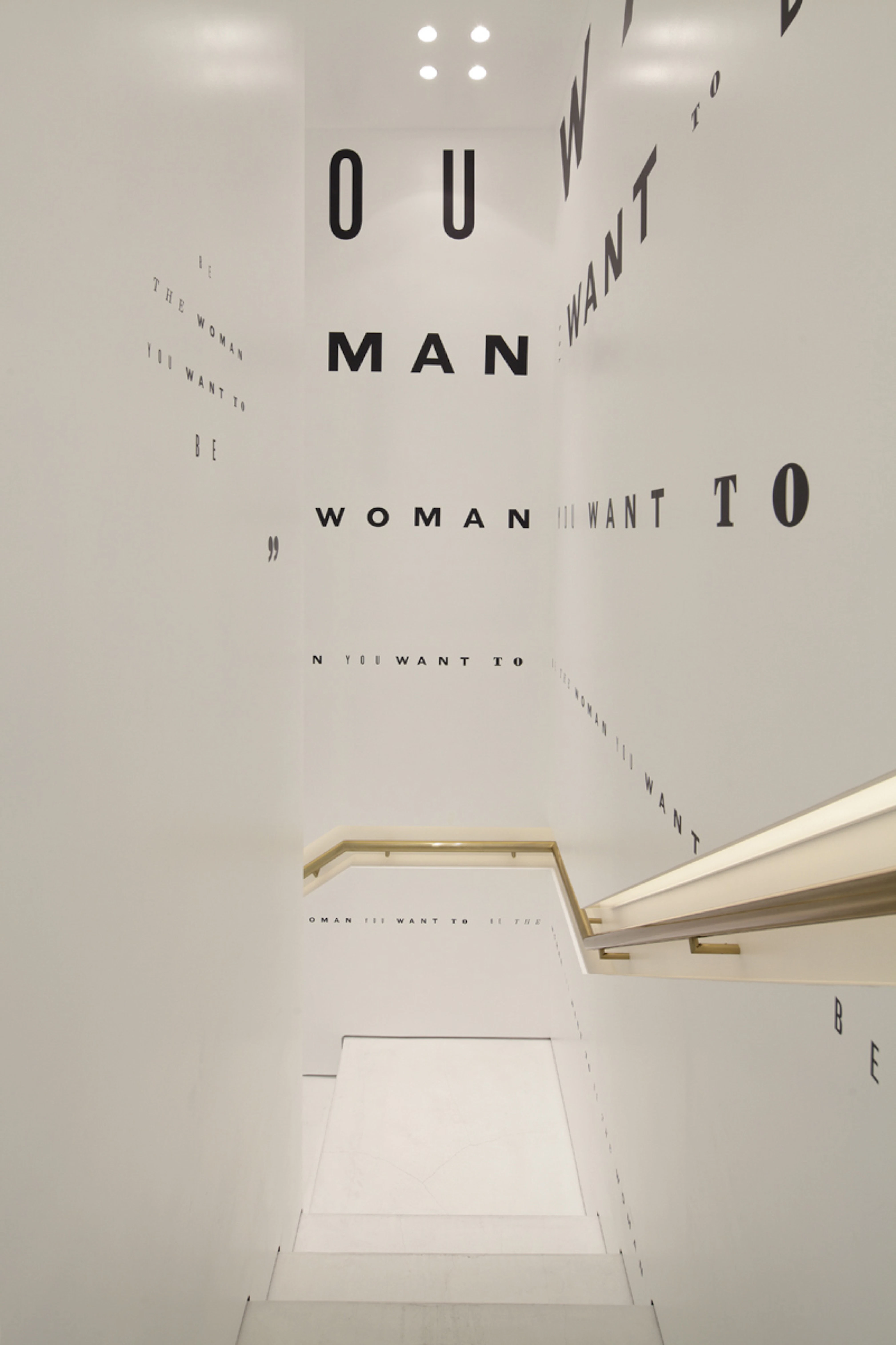 Image from the inside of the DVF store in Tokyo showing the staircase with mantras written all over the white walls in black type of different sizes.