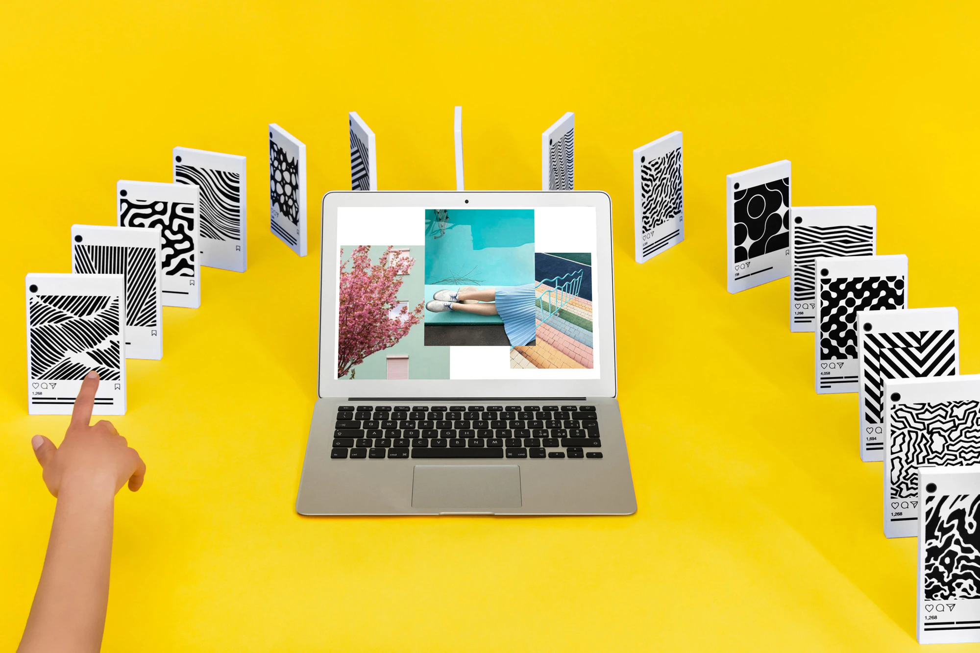 Image shows a laptop sitting on a yellow background surrounded by an arch of 3D phone screens, set up like dominoes with a hand reaching in as though it would knock over the first in the row.