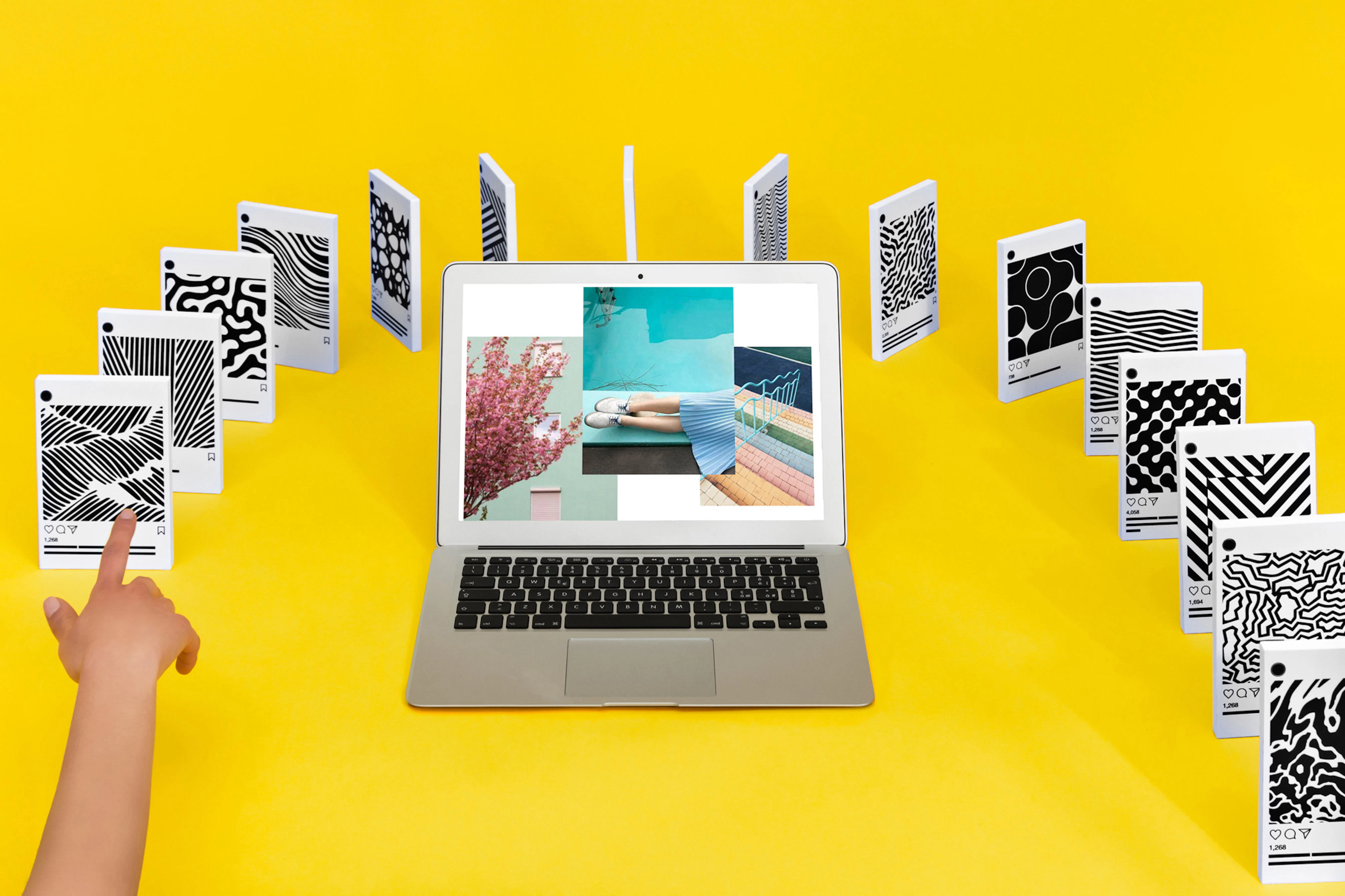 Image shows a laptop sitting on a yellow background surrounded by an arch of 3D phone screens, set up like dominoes with a hand reaching in as though it would knock over the first in the row. 