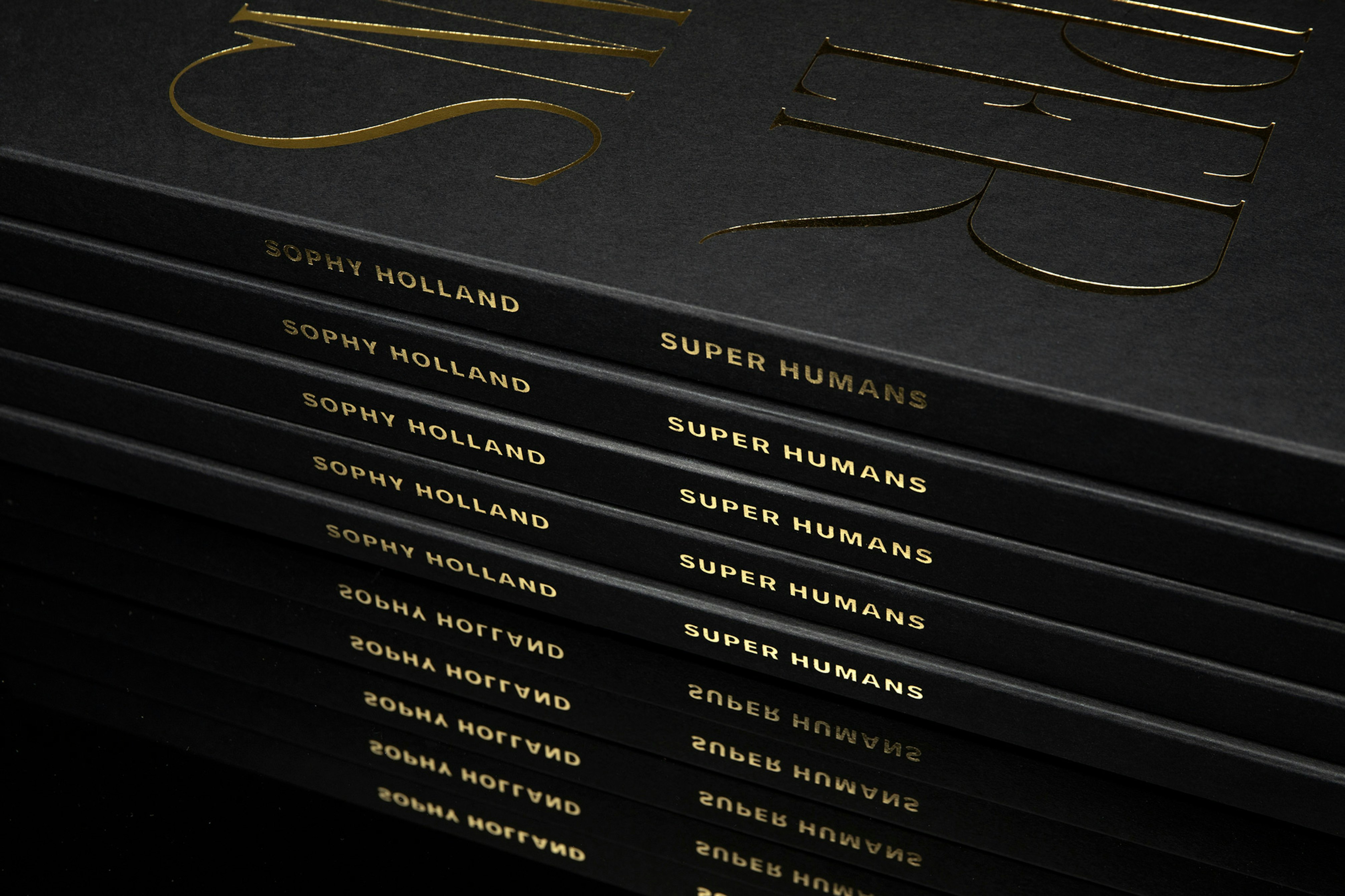 Image shows a black stack of books with gold text on the spine reading SOPHY HOLLAND SUPER HUMANS.