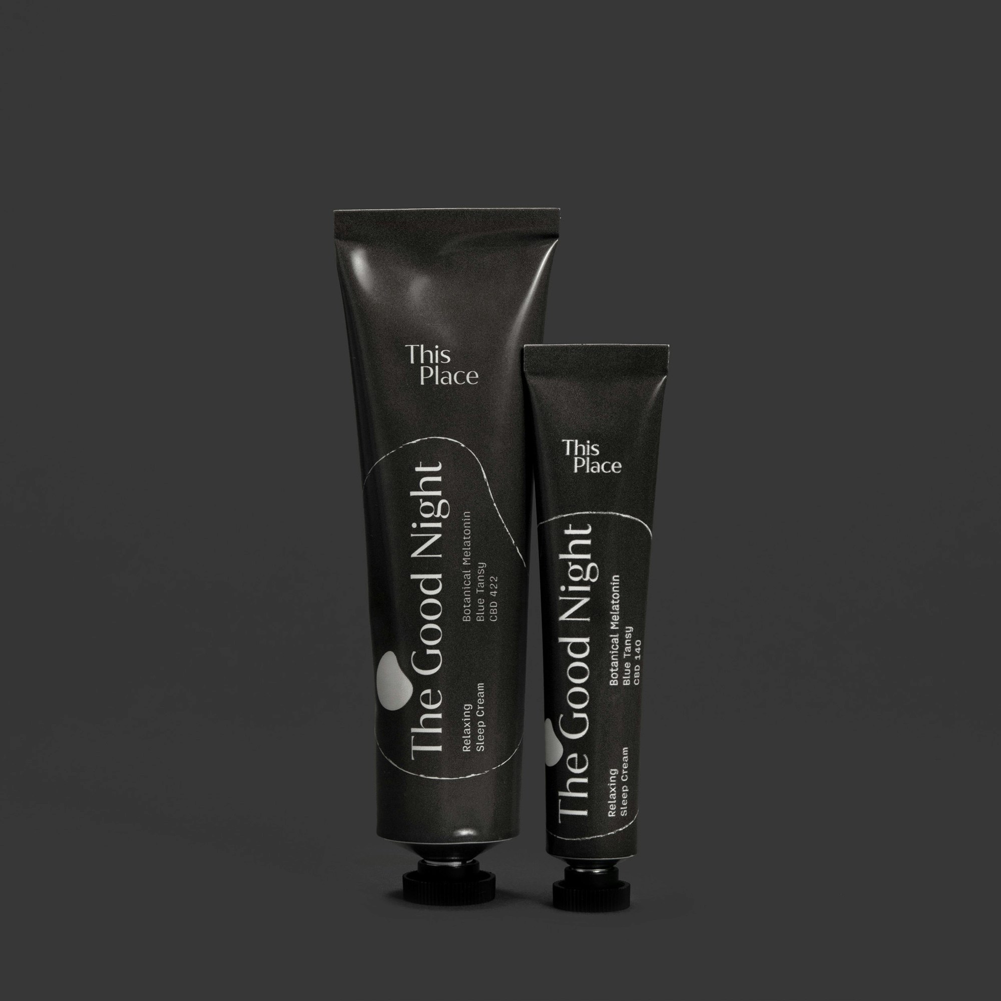 Two charcoal colored tubes standing on a charcoal seamless. The Good Night is written across the tubes in cream type.