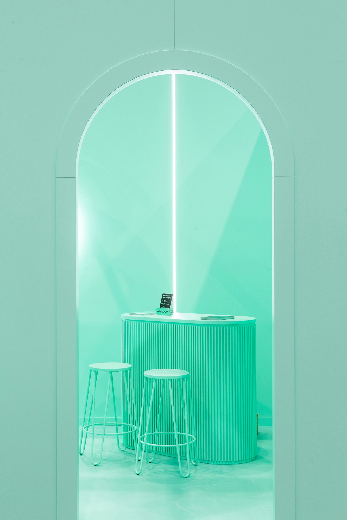 Image showing one of the two arched entrances to the Afterpay Bondi Mint expo booth. Looking through the entrance we can see a tall mint desk with two mint stools in front of it. On top of the desk are black pamphlets explaining Afterpay.