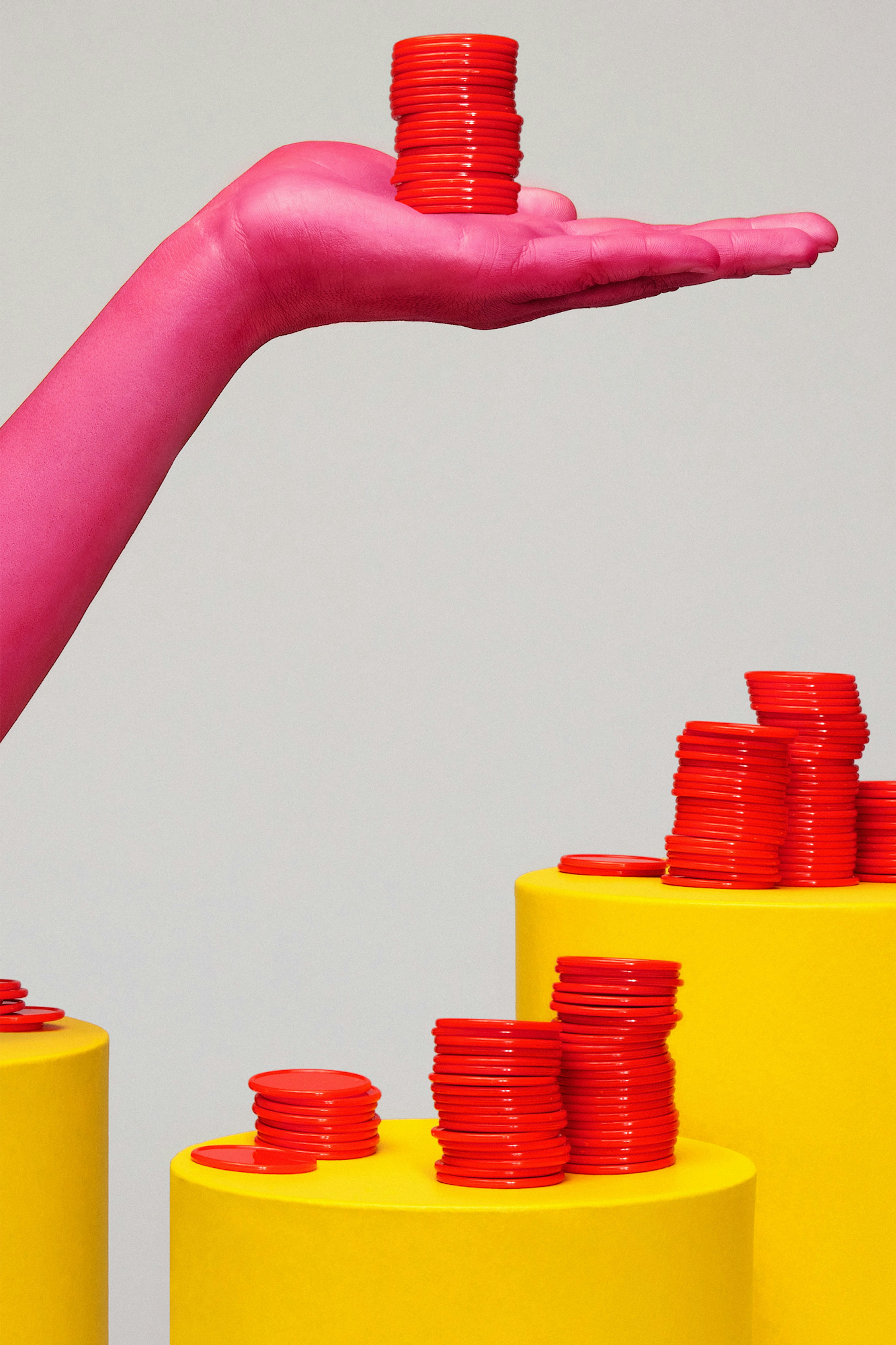 A pink hand holds a stack of red coins above yellow pedestals with more stacks of red coins on them. 