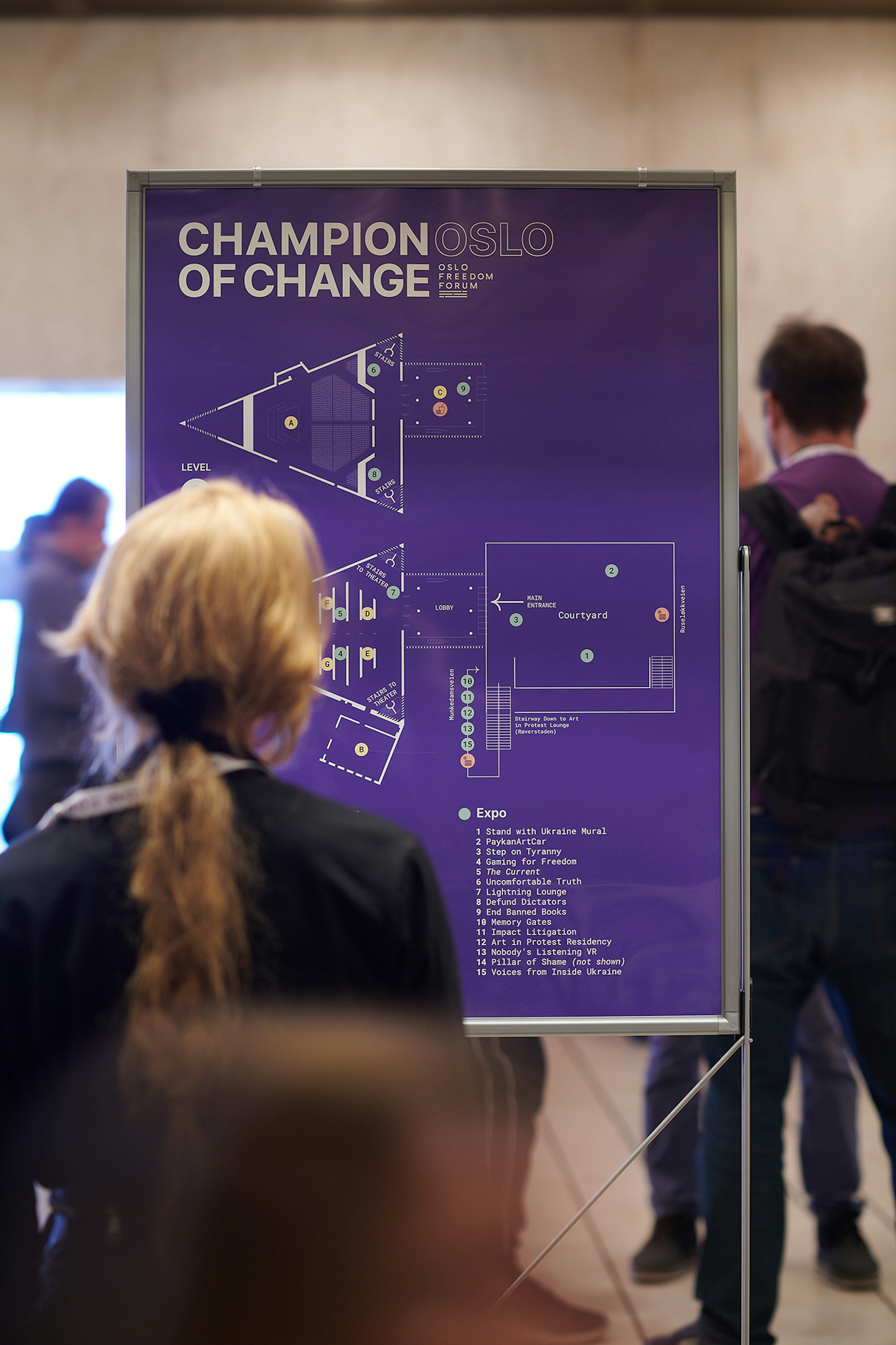 The image showing a map of two stories of the konserthus in white on a purple background. There's a person looking at it in front.