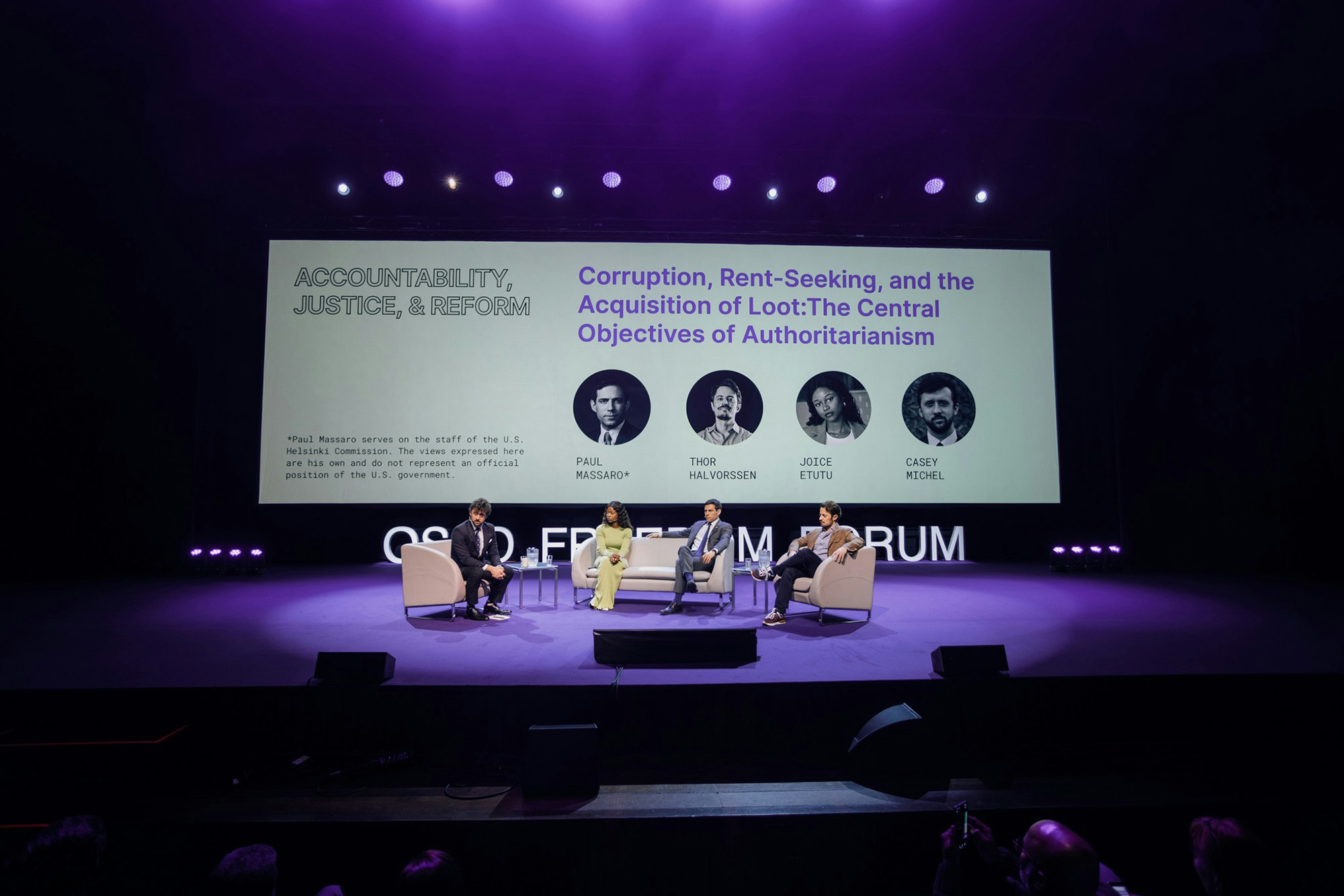 There're four people on the stage sitting on chairs talking to each other. The screen behind saying "Accountability, Justice, & reform. Corruption, Rent-Seeking, and the Acquisition of Loot: The Central Objective of Authoritarianism. Paul Massaro (serves on the staff of the US Helsinki Commission. The views expressed here are his own and do not represent an official position of the US government), Thor Halvorssen, Joice Etutu, Casey Michel."