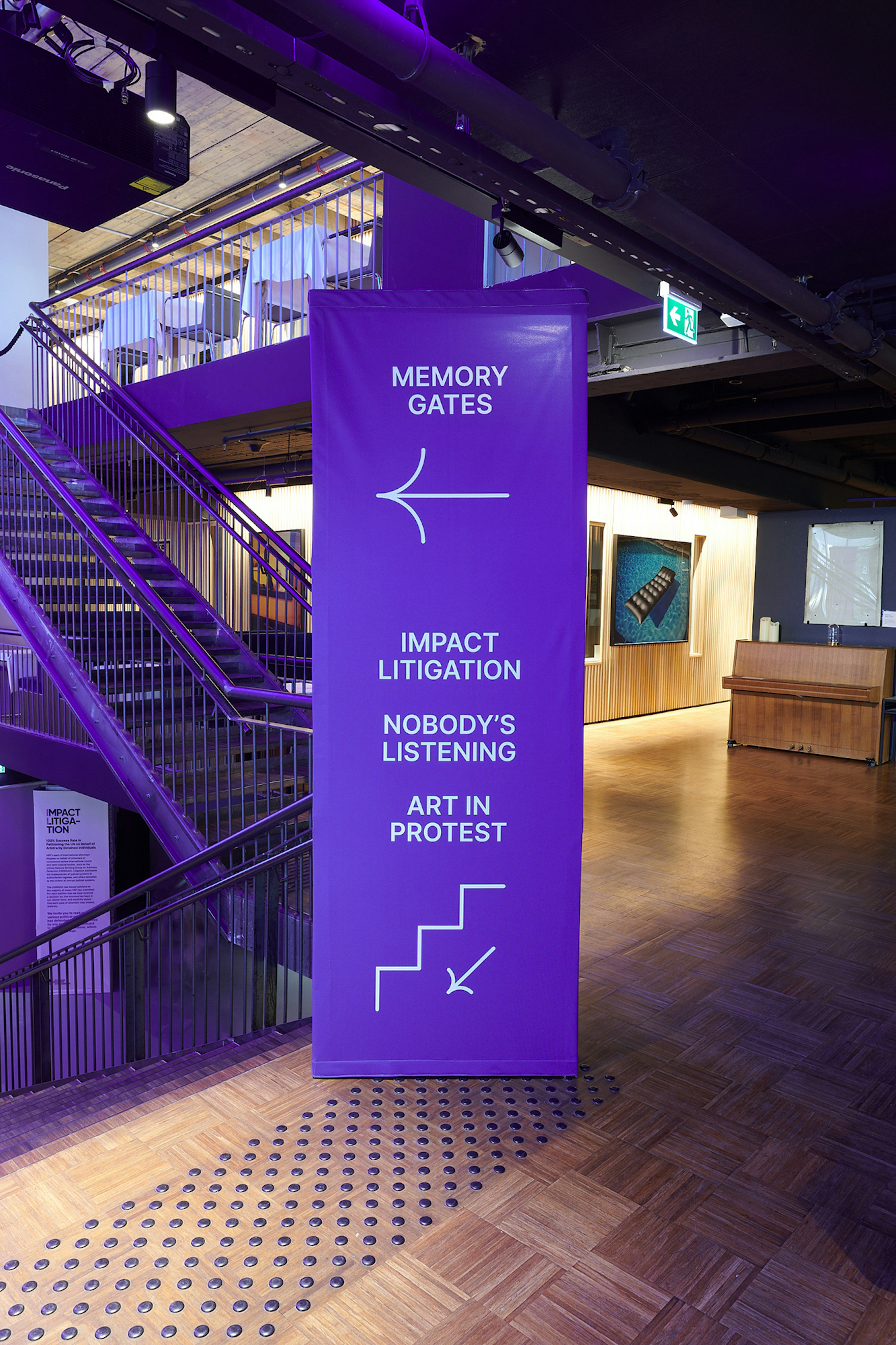 Way-finding hop up that pointing left to Memory Gates and pointing down stair for Impact Litigation, Nobody's Listening, and Art in Protest.