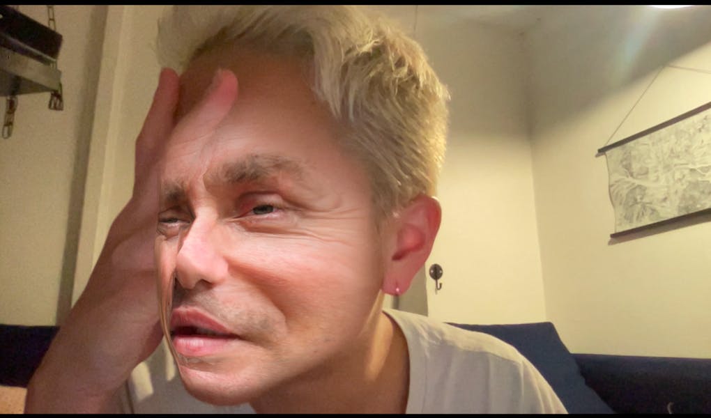 Face filter of a caucasian man's face over the artist's face. A hand is placed over the face, warping the features