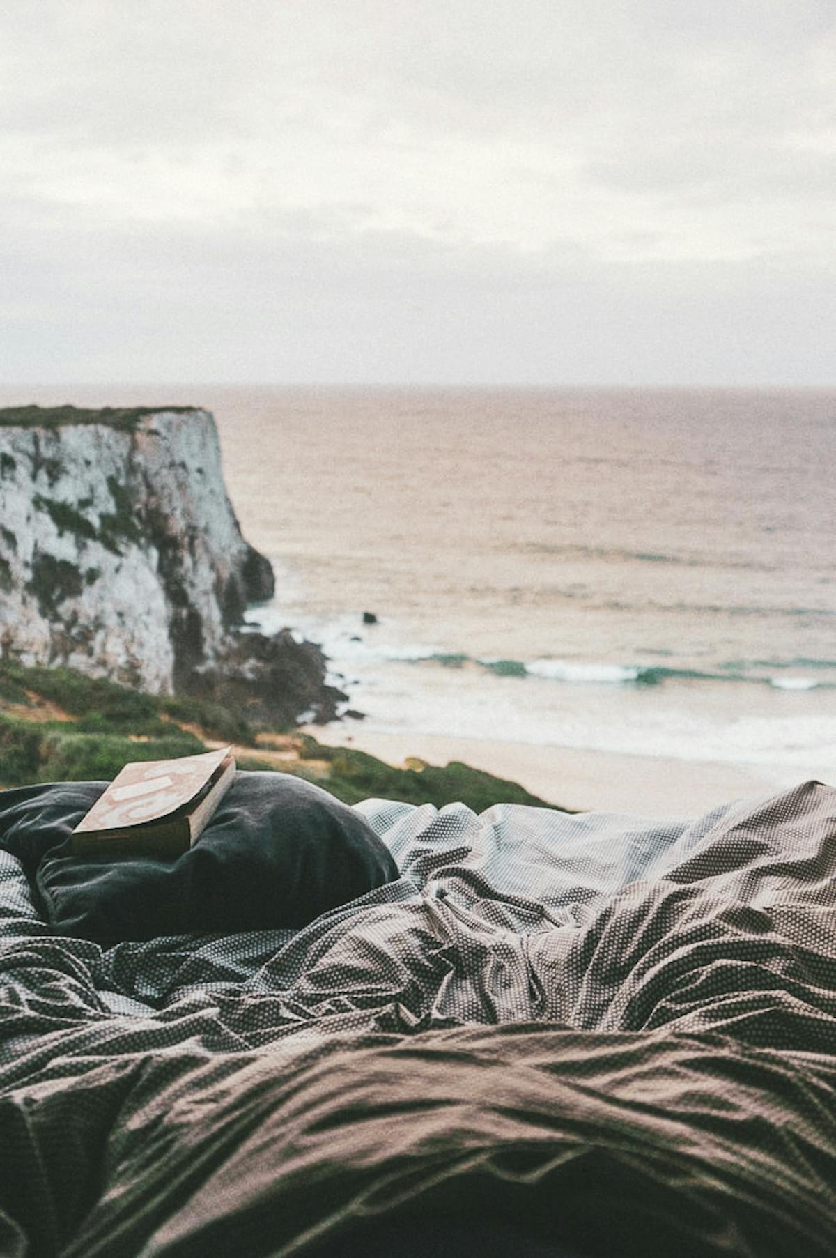 Book on a bed facing a cliff overlooking the sea