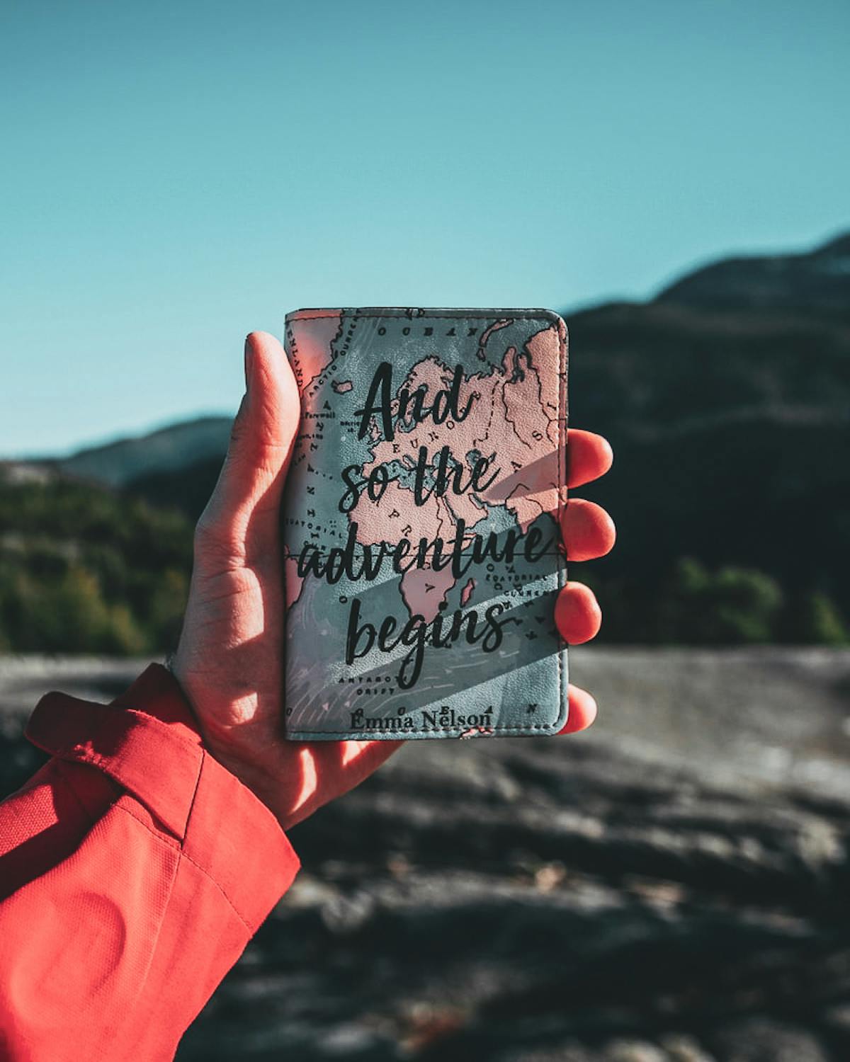Hand holding a passport holder facing mountains