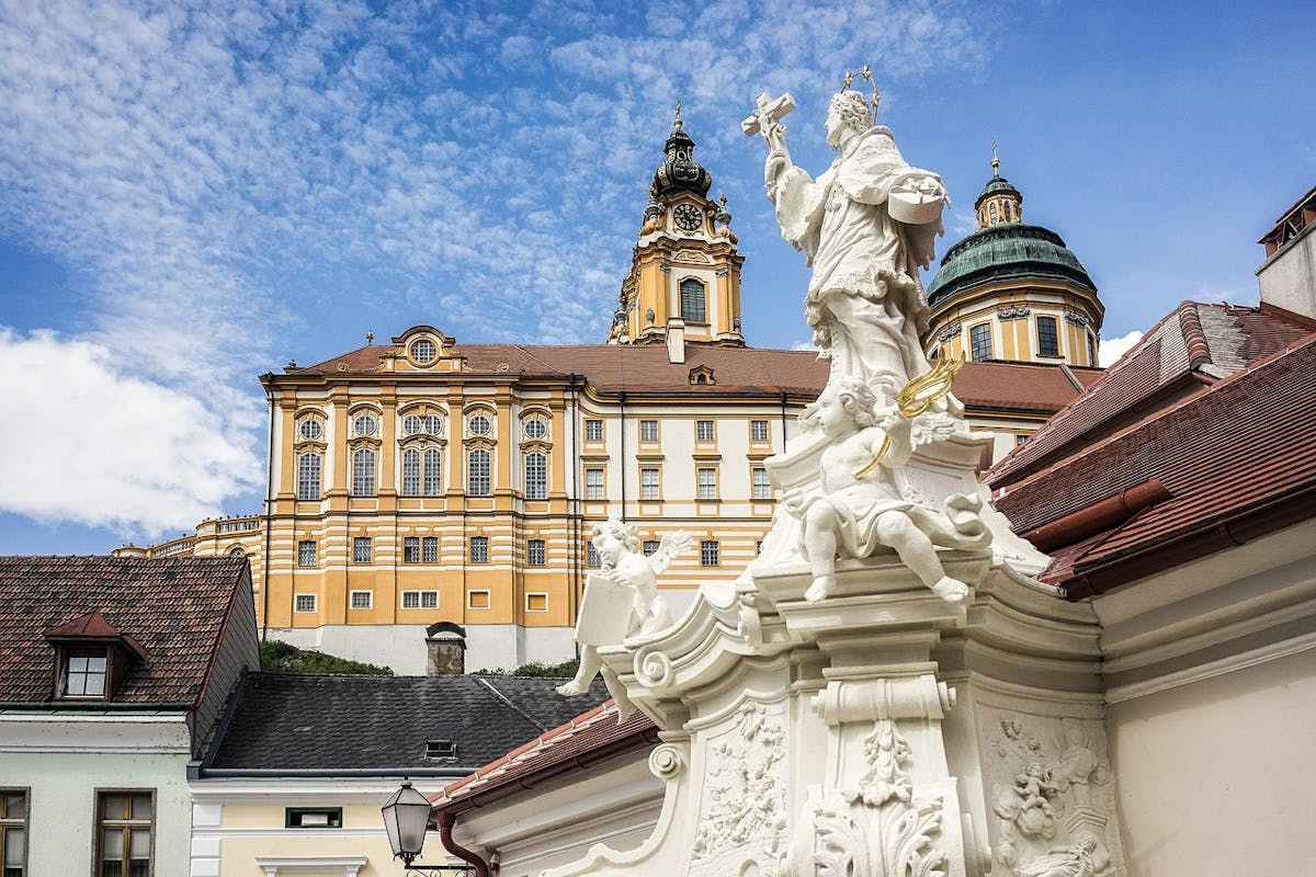Photo of a golden-coloured abbey, with a religious statue in the foreground