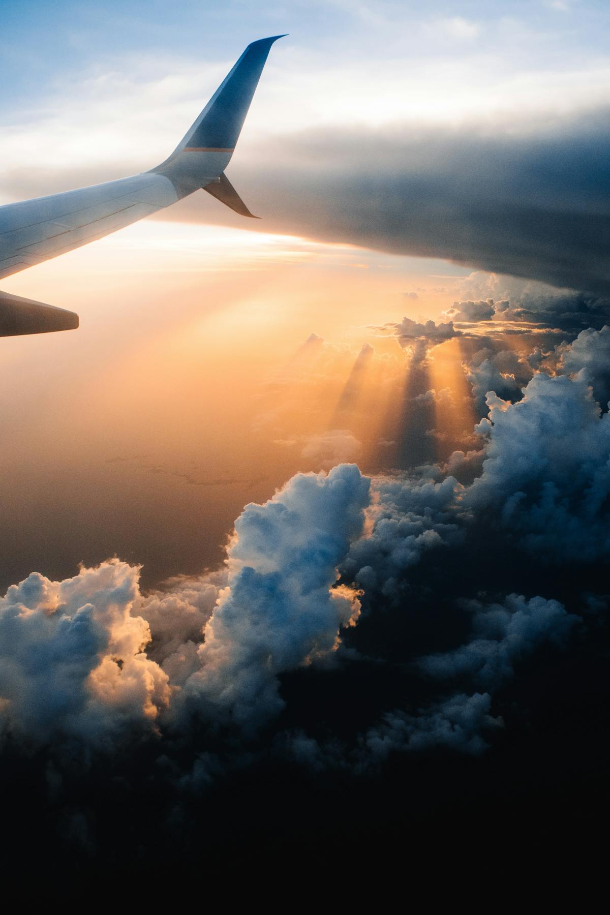 Seen from a window, the setting sun behind the clouds and the right wing of a plane - Photo by Tom Barrett on Unsplash