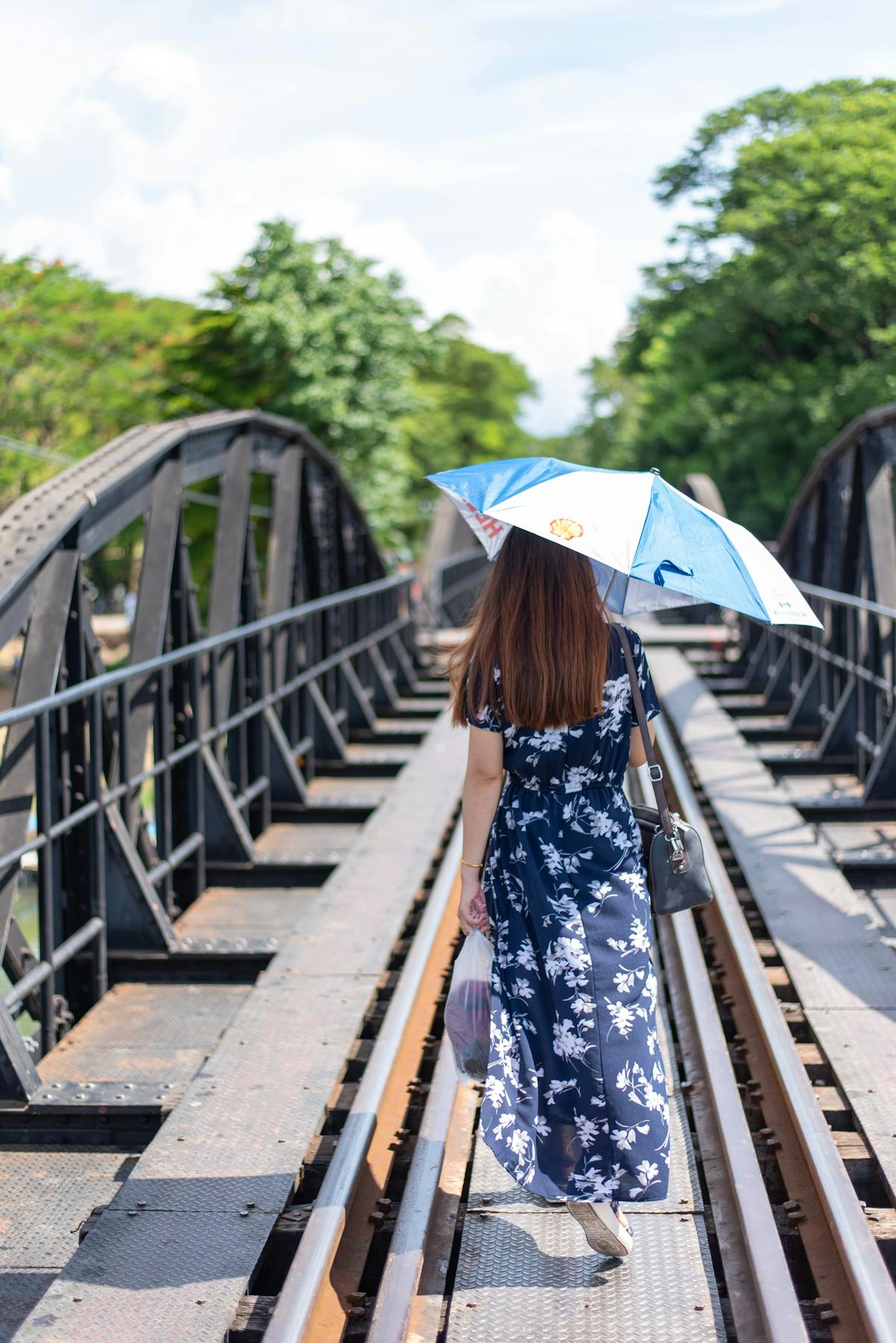 A young woman with an umbrella walks on the bridge of the river Kwai - Photo by mistermon on Unsplash