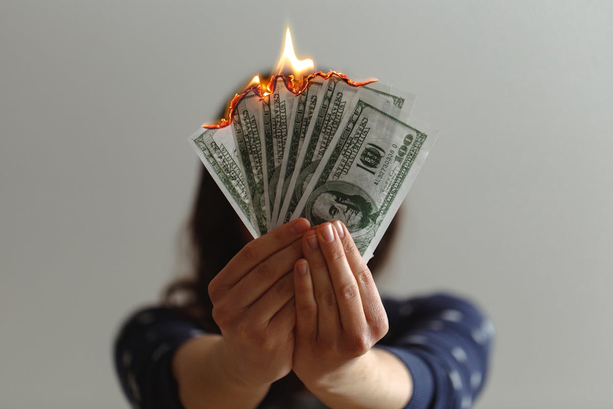 A young brown woman holds a fan of burning banknotes - Photo by Jp Valery on Unsplash