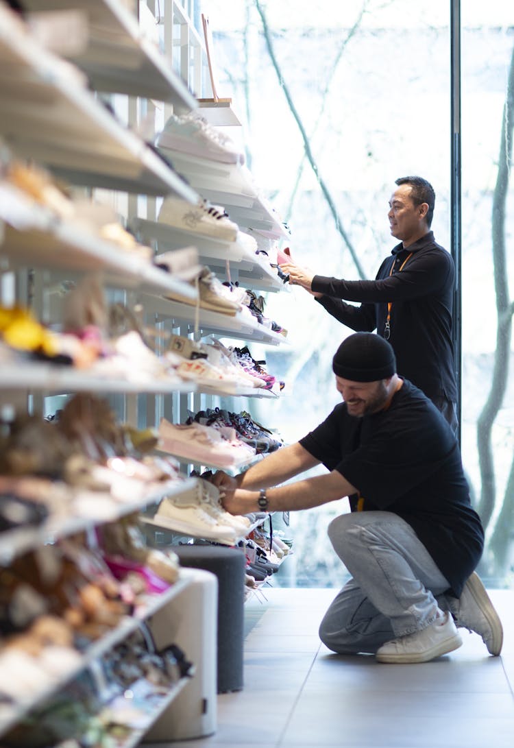 Two people arrange shoes on a shelf and smile