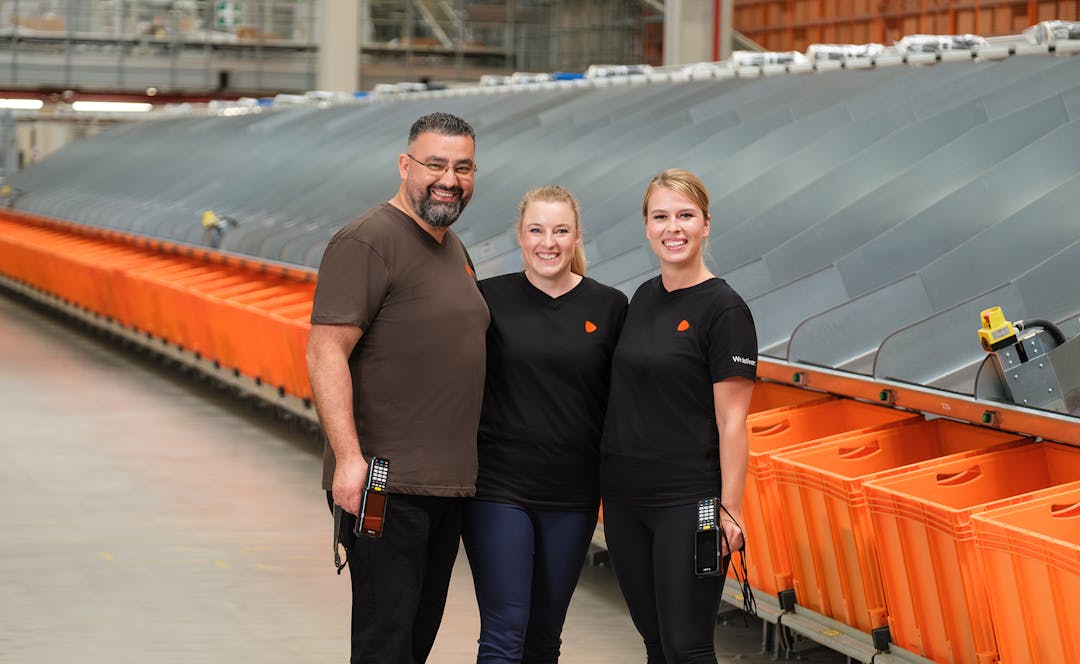 Three people standing in a logistic warehouse with two of them holding scanners.