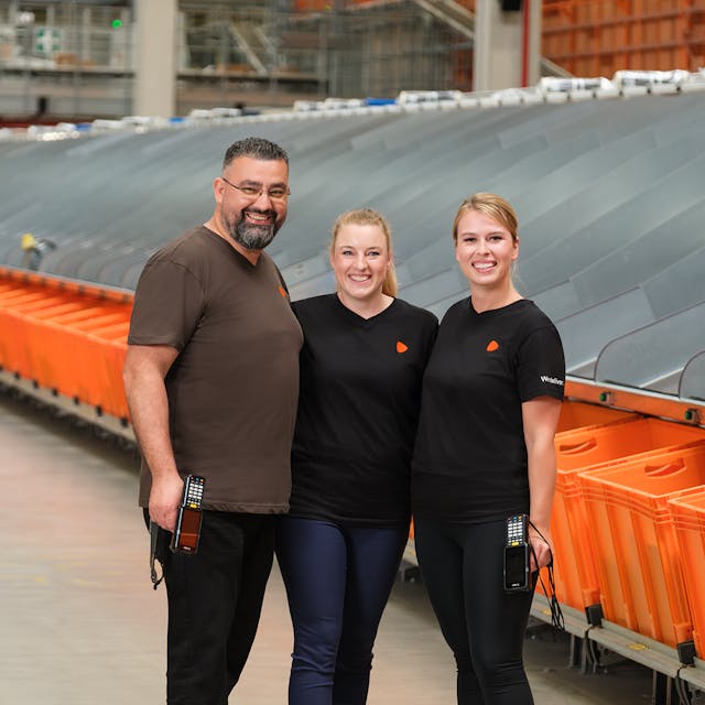 Three people standing in a logistic warehouse with two of them holding scanners.