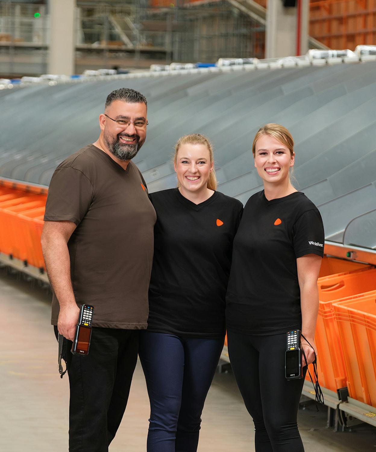 Three people standing in a logistic warehouse with two of them holding scanners.