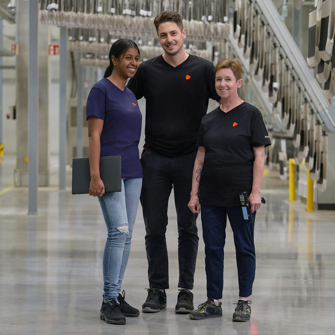 Three people standing as a team in a warehouse. One holding a laptop and one is holding a scanner.