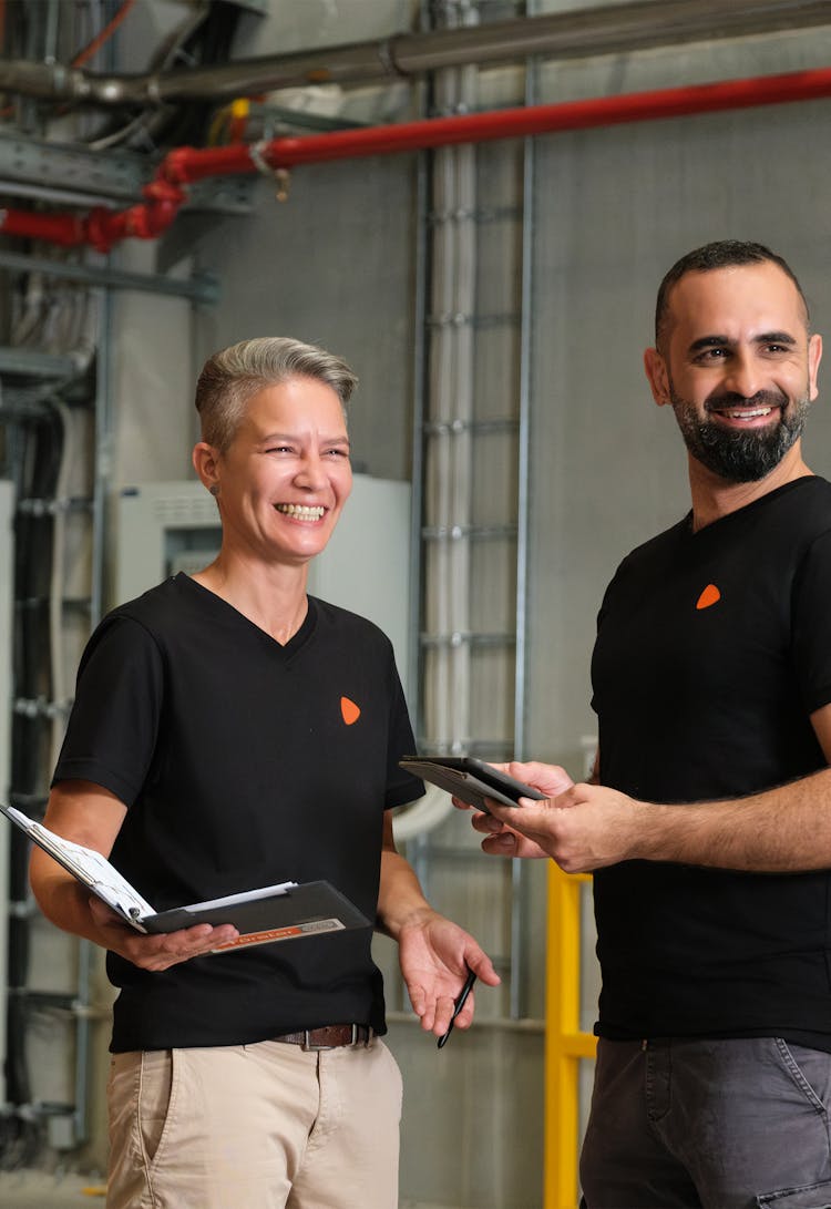 Two people standing, one is documenting while the other is checking their tablet, in a logistics warehouse.