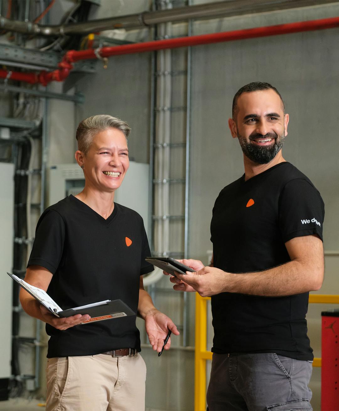 Two people standing, one is documenting while the other is checking their tablet, in a logistics warehouse.