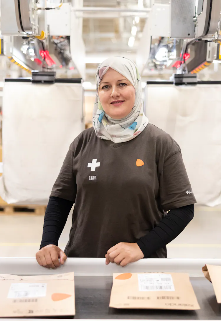 A woman standing at a logistics centre before packages on a conveyor belt.
