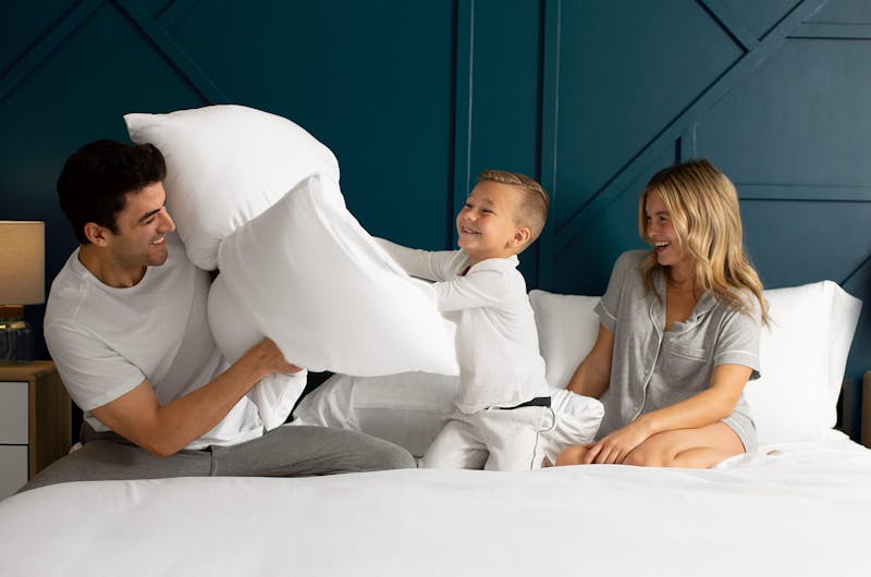 A child having a pillow fight with his parents on a bed