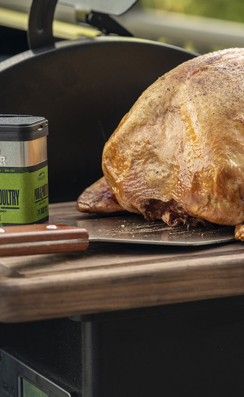 A turkey sitting on a Traeger grill next to some pork and poultry rub.