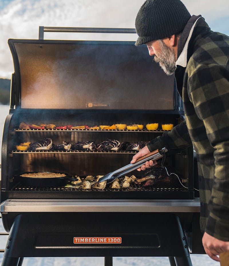 A man grilling vegetables in the winter on a Traeger