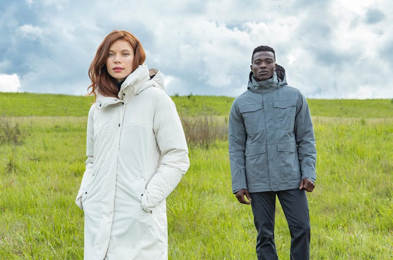 A man and a woman standing in a field wearing jackets