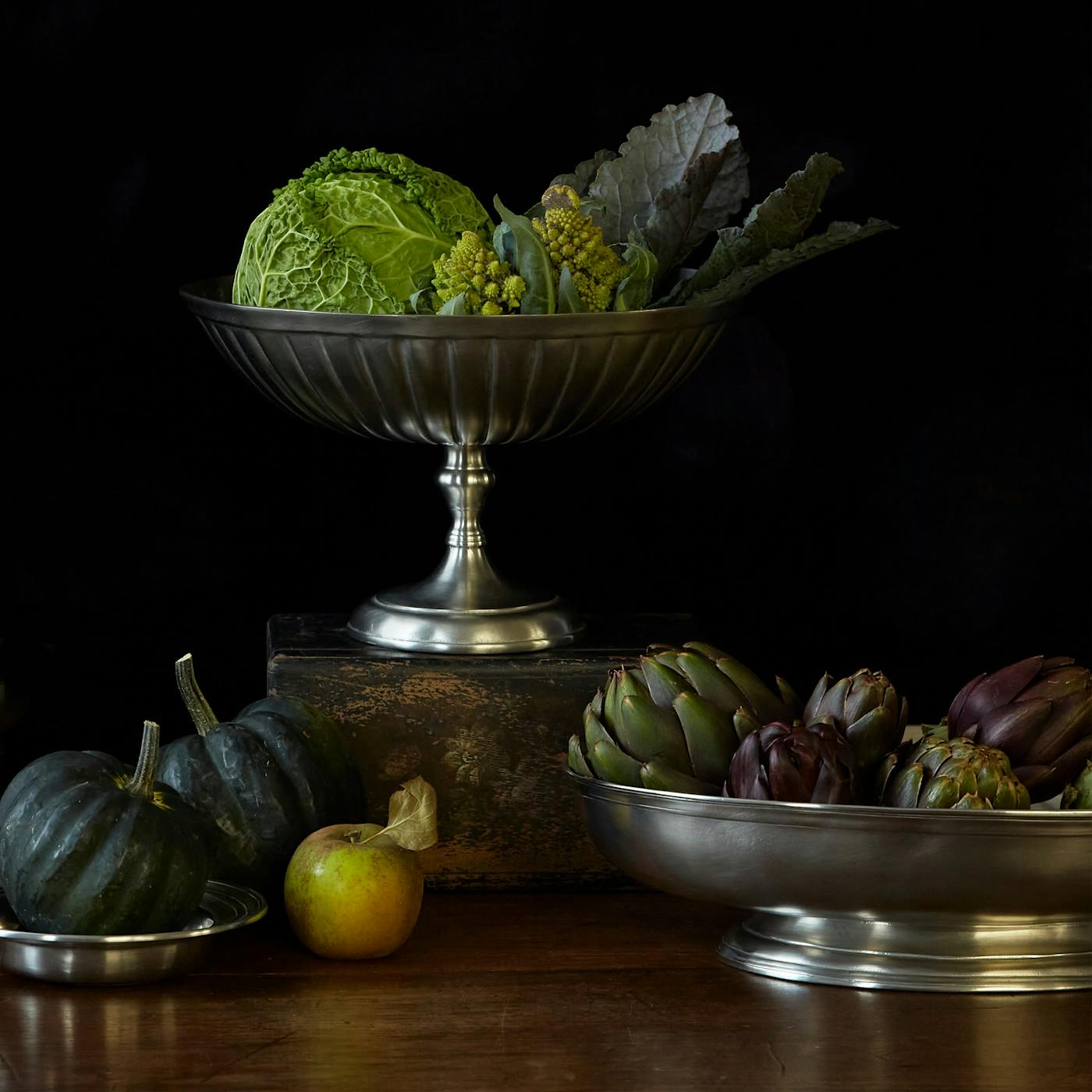 A still life of Match Pewter serveware with vegetables inside.