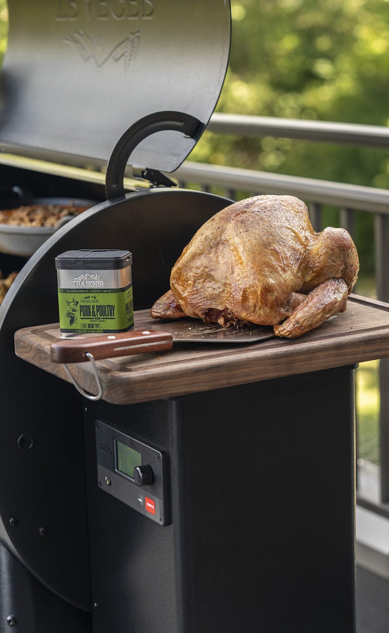 A turkey sitting on a Traeger grill next to some pork and poultry rub.