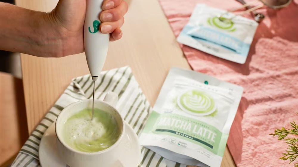 Person frothing matcha in a teacup with Jade Leaf product packages to the side