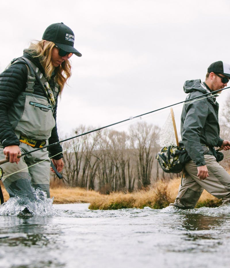 A man and a woman walking through a lake with fly fishing gear
