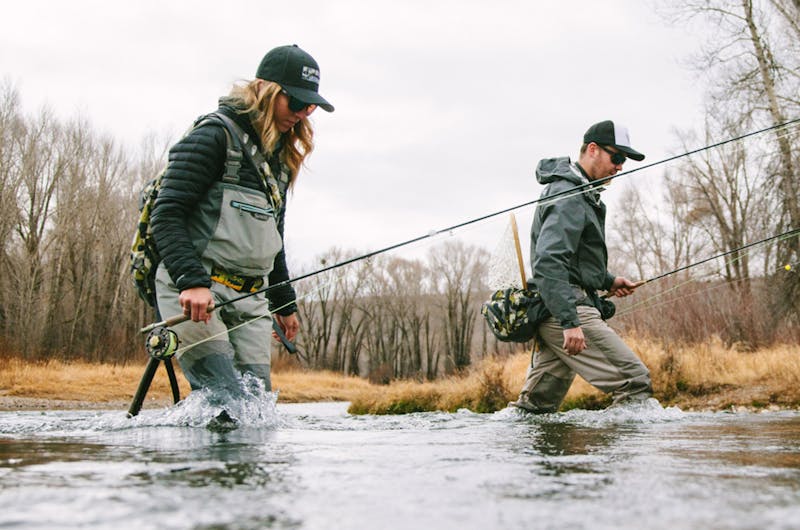 A man and a woman walking through a lake with fly fishing gear