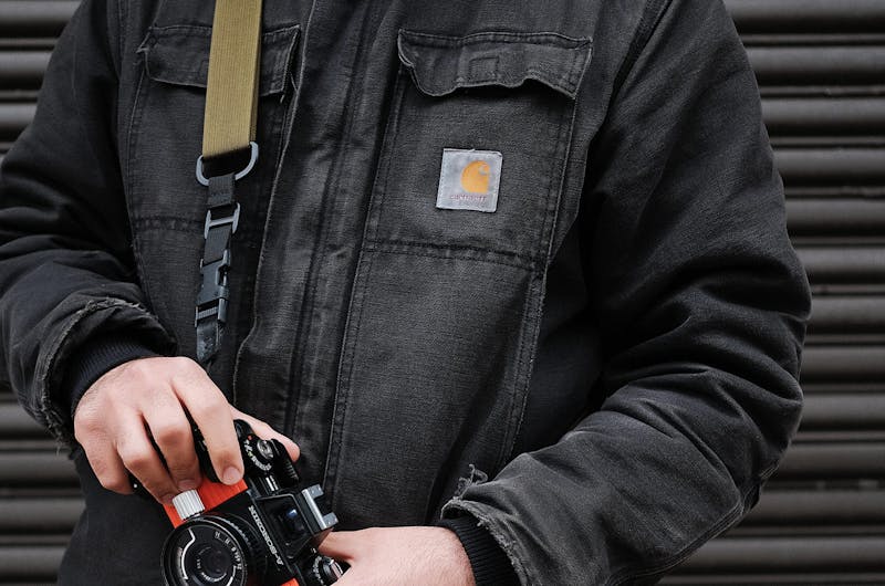Man wearing a black denim Carhartt jacket and holding a camera