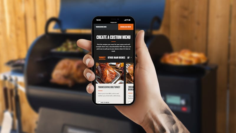A hand holding an iPhone with the Traeger Thanksgiving page on the screen.