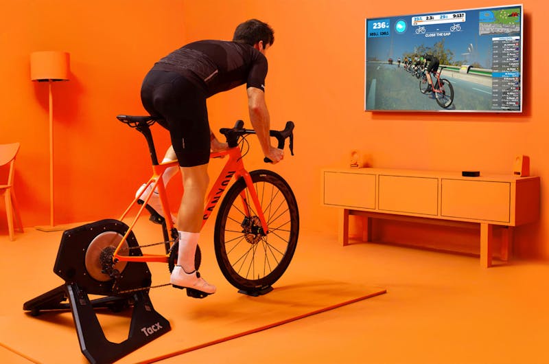 A man riding a workout bike while watching the Zwift exercise app on his TV