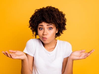 Mulher com as mãos levantas ao meio do corpo com a expressão e sinalizando dúvida.