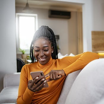 mulher sorridente sentada no sofá com o celular nas mãos