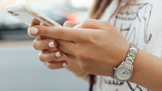 Mãos femininas utilizando um aparelho celular.