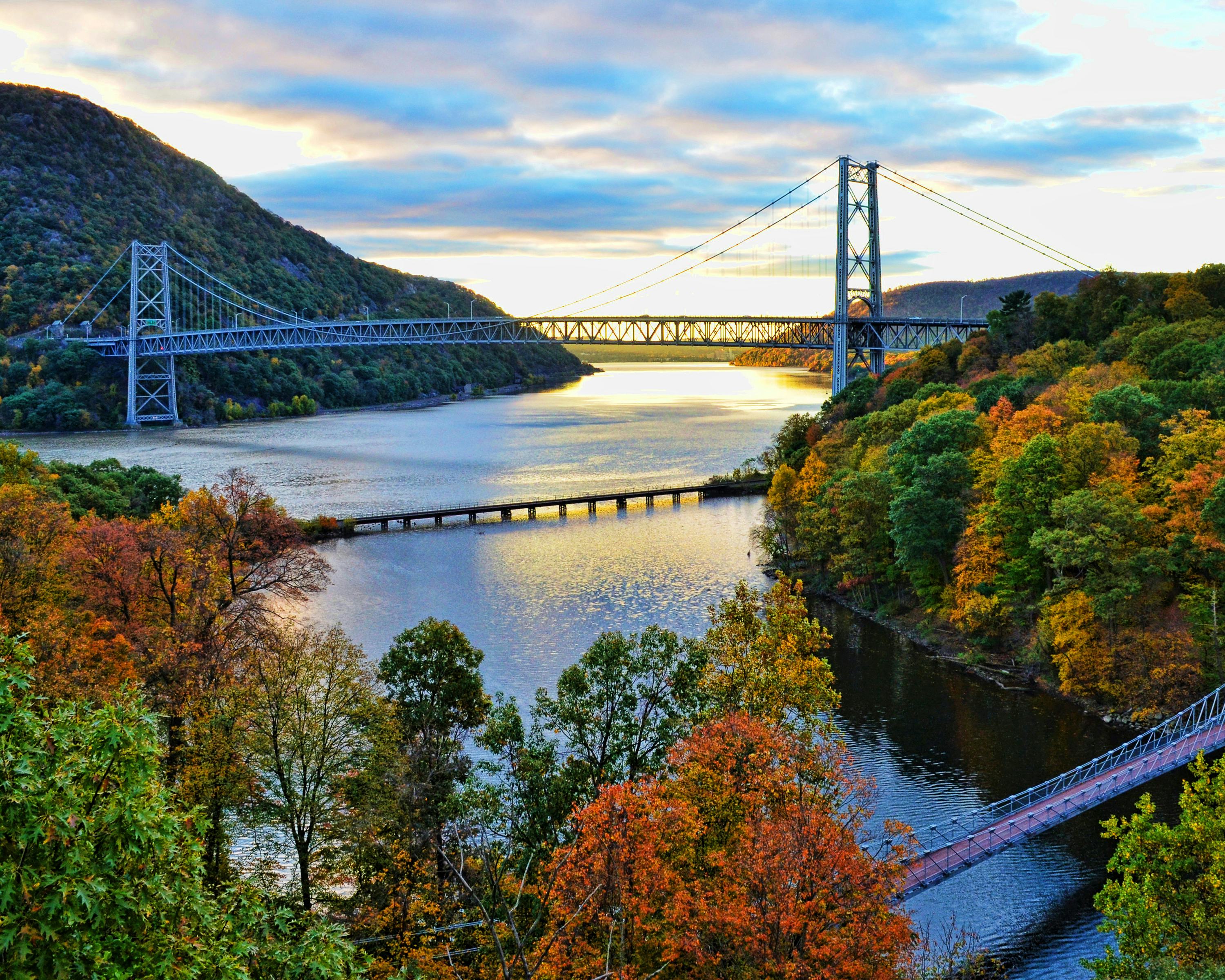 Bear Mountain Bridge in Hudson Valley, New York during sunrise with colorful trees around it. 