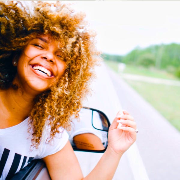 Woman with luscious curly hair smiling with her head out a car window